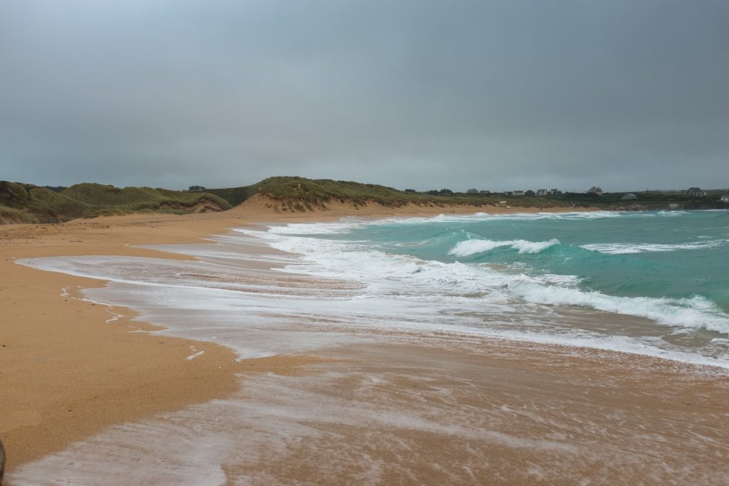 Rolling waves along Constantine Beach with overcast grey sky.